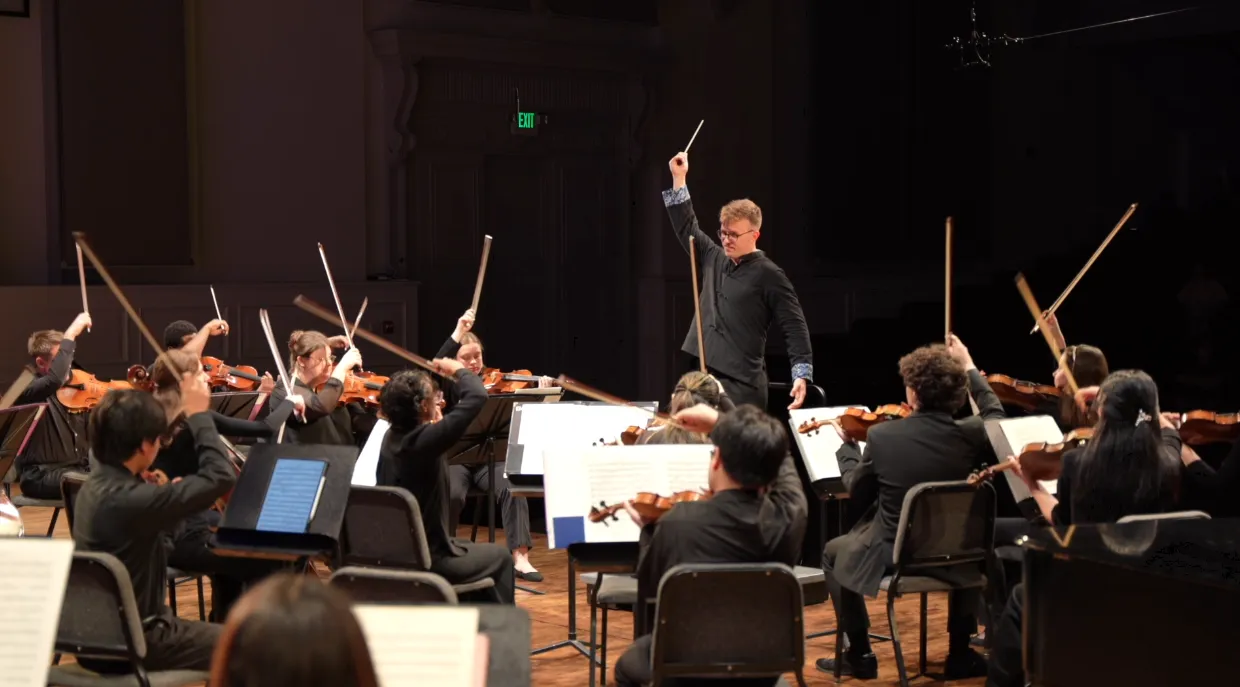 Alon Ben Dor conducting a string orchestra with bows raised